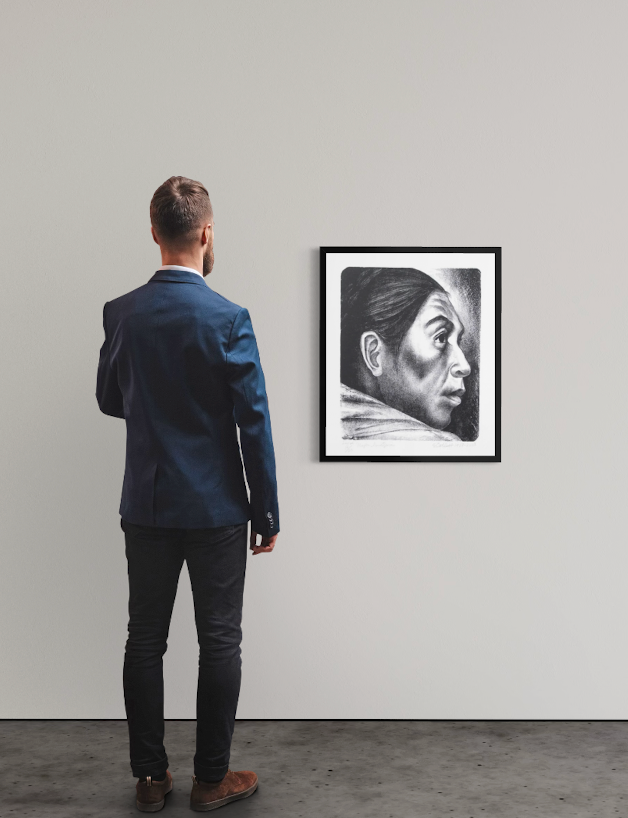 <img alt="Installation view of Elizabeth Catlett's Cabeza Indígena, framed work hanging on a white gallery wall, with a visitor standing with their back to the camera contemplating the piece." />
